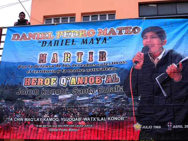 A banner memorializing Daniel Pedro Mateo is displayed at a protest in the central park of Santa Cruz Barillas on March 14, 2014. Mateo, an indigenous leader who opposed local dam projects, was abducted and killed nearly a year earlier, and his body was found with signs of torture. The banner refers to him as a martyr and hero for the defense of collective rights, the territory, and Mother Nature, and quotes him saying "If they kill me, let it be for a just cause." Photo credit: Luis Miranda Brugo / Alba Sud Fotografia.